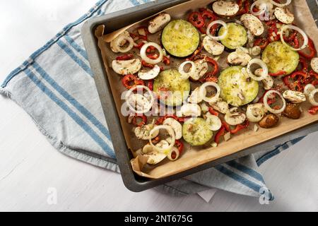 Gemüse mit Kräutern und Gewürzen auf einem Backblech, blaues Handtuch und weißer Tisch, mediterrane vegetarische Vorspeise, Kopierbereich, Blick aus einem hohen Winkel von ab Stockfoto