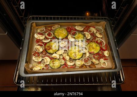 Gebackenes Gemüse mit mediterranen Kräutern und Gewürzen auf dem Tablett, frisch aus dem dunklen Ofen, vegetarische Mahlzeit, ausgewählter Fokus, schmale Feldtiefe Stockfoto