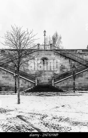 Historische Steintreppe von der Kampa-Insel zur Karlsbrücke in Prag, Tschechische Republik. Die Winterlandschaft verschönert die malerische Aussicht. Schwarzweißfotografie. Stockfoto