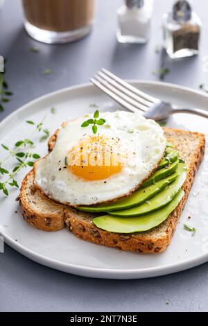 Avocado-Toast mit Vollkorn und Spiegelei auf der Oberseite, gesunde Frühstücksidee Stockfoto