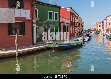 Festgemachte Boote auf dem Kanal, gesäumt von bunten Häusern und Geschäften plus hölzerne Fußgängerbrücke, Burano Island, venezianische Lagune, Venedig, Venetien, Italien. Stockfoto