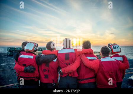 Auf See. 22. Februar 2023. Seeleute beobachten den Sonnenuntergang auf dem Flugdeck an Bord des Flugzeugträgers USS Dwight D. Eisenhower (CVN 69) der Nimitz-Klasse nach einer Munition mit dem Trockenfracht- und Munitionsschiff USNS Medgar Evers (T-AKE 13). IKE führt derzeit im Rahmen seiner maßgeschneiderten Grundphase vor dem Einsatz Munition Onload, Cockpit-Zertifizierung und Luftflügelqualifizierung durch. Kredit: USA Navy/ZUMA Press Wire Service/ZUMAPRESS.com/Alamy Live News Stockfoto