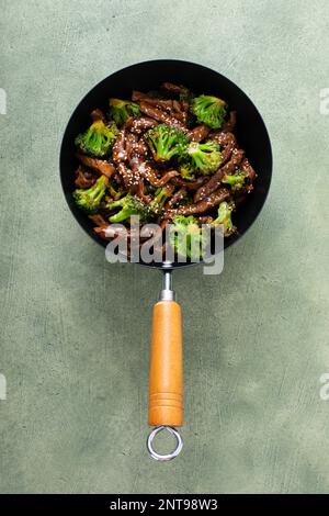 Rind und Brokkoli in einem kleinen Wok über dem grünen Hintergrund Stockfoto