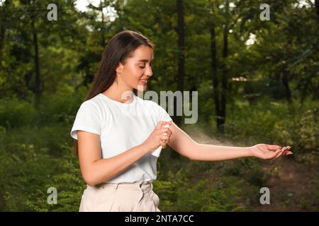 Frau, die im Park Insektenschutzmittel auf den Arm aufträgt. Zeckenbissprophylaxe Stockfoto