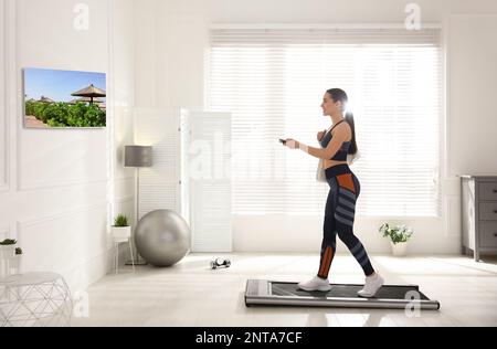 Sportliche Frau mit Fernbedienungstraining auf Laufband und Fernsehen zu Hause Stockfoto