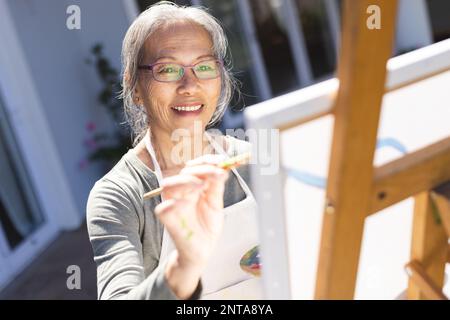 Glückliche ältere asiatische Frau, die im Garten auf Staffelei malt Stockfoto