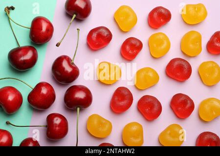 Köstliche gummierte Kirschbonbons und frisches Obst auf farbigem Hintergrund, flach liegend Stockfoto