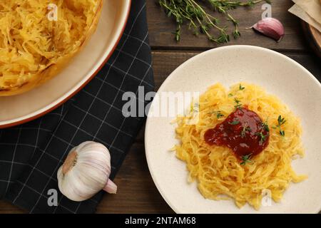 Leckerer Spaghetti-Kürbis mit Tomatensoße und Thymian, serviert auf einem Holztisch, flach liegend Stockfoto