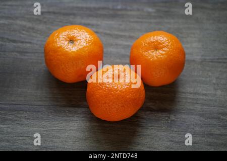 Ganze drei Klementinen oder Mandarinen auf rustikalen Holztisch mit geringer Tiefenschärfe Stockfoto