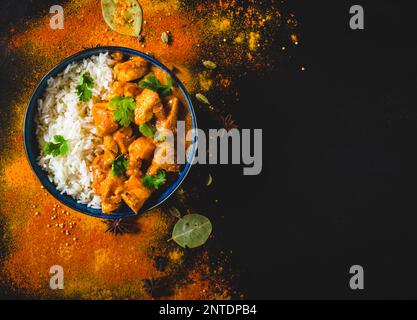 Indisches Butterhuhn mit Basmati-Reis in Schüssel, Gewürze, schwarzer Hintergrund. Platz für Text. Butterhähnchen, traditionelles indisches Gericht. Draufsicht. Hühnchen Stockfoto