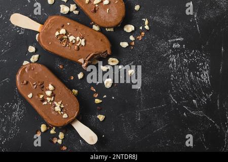 Milchschokolade Eis am Stiel mit Haselnüssen. Nahaufnahme. Eis am Stiel bedeckt mit Schokolade, Stöcken und schwarzem Steinmarmorhintergrund. Platz für Text. Stockfoto