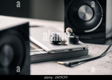 Ein Paar schwarze, echte schnurlose Ohrstöpsel mit Smartphone. Entspannungskonzept. Stockfoto