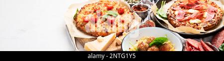 Tisch mit italienischen Gerichten auf Tellern und Brett - Pizza, Pasta, Fleischbällchen, Salami, Parmesan, Oliven, Brotstangen auf weißem Hintergrund. Draufsicht. Pa Stockfoto