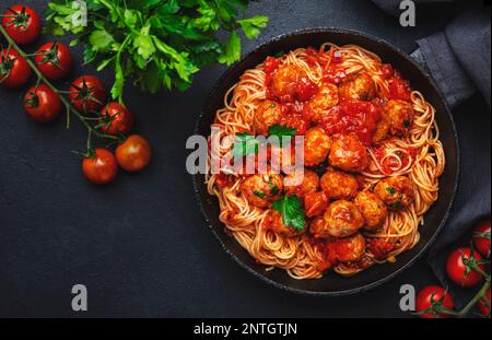 Spaghetti-Pasta mit Fleischbällchen in Tomatensoße mit Petersilie in der Pfanne, dunkler Tischhintergrund, Draufsicht Stockfoto