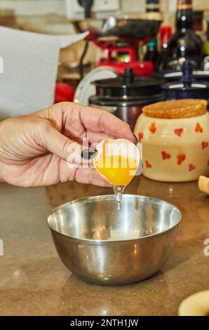 Der Koch knackt ein Ei in ein Gericht, das in einer Schüssel zubereitet wird Stockfoto