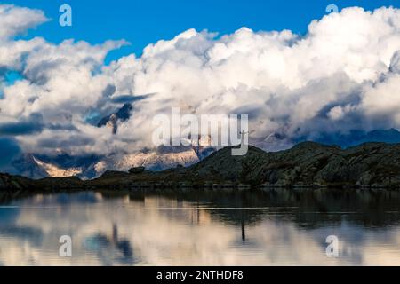 Ein Mann, der auf einem felsigen Hügel am Lago Nero-See steht, der Hauptanlage der Brenta-Dolomiten, teilweise von Sturmwolken umhüllt, in der Ferne. Stockfoto