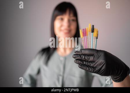 Kosmetiker mit Bürsten zur Wimpernverlängerung auf grauem Hintergrund. Bürste zum Glätten von Wimpern und Augenbrauen. Speicherplatz kopieren Stockfoto