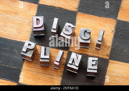 Disziplin-Wort aus verstreuter metallischer Schrift auf Holzschachbrett Stockfoto