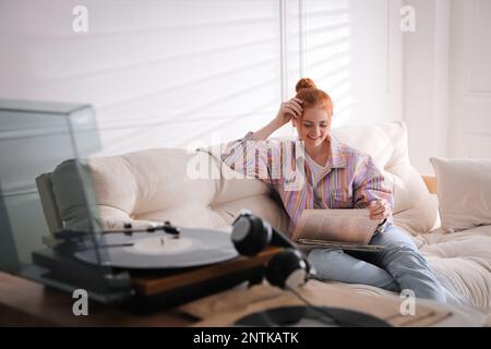 Junge Frau, die sich für eine Vinyl-Disc entscheidet, um zu Hause Musik mit dem Plattenspieler wiederzugeben Stockfoto