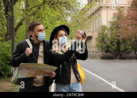 Ein paar Touristen in medizinischen Masken mit Karte und Kamera auf der Straße der Stadt Stockfoto