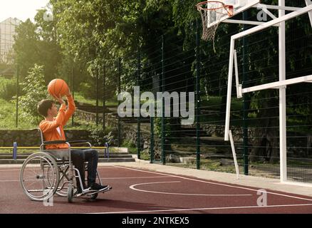 Behinderter Teenager im Rollstuhl, der Basketball auf dem Spielfeld spielt Stockfoto