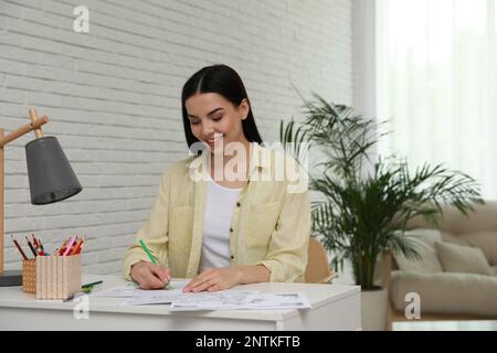 Eine junge Frau, die eine Anti-Stress-Seite am Schreibtisch im Haus ausmalt Stockfoto