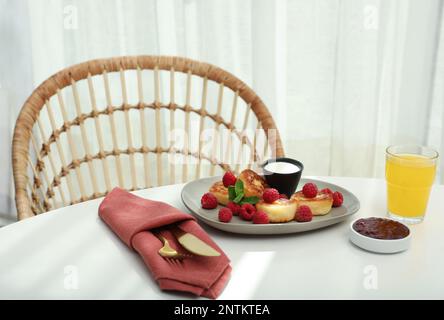 Köstliche Hüttenkäse-Pfannkuchen mit frischen Himbeeren, saurer Sahne und Minze, serviert auf einem weißen Tisch im Haus Stockfoto