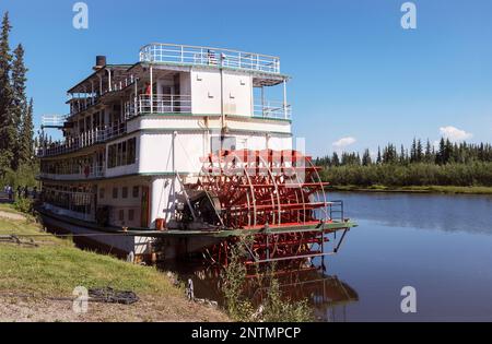 Touristen steigen in ein Sternradboot und fahren auf dem Chena River in der Nähe von Fairbanks in Alaska mit Fluss und Wald und blauem Himmel im Hintergrund Stockfoto