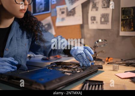 Frau, die das Notebook-Motherboard demontiert, installieren Sie das Speicherboard. Ingenieur repariert defekten Computer bei der Arbeit in einer Computerreparaturwerkstatt. Elektro Stockfoto