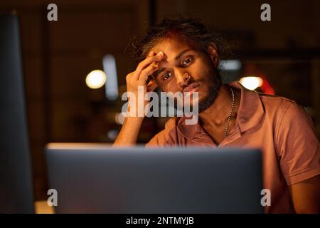 Ein müder Programmierer, der an einem neuen Programm arbeitet, sitzt am Arbeitsplatz vor dem Computer und arbeitet bis spät in die Nacht im IT-Büro Stockfoto