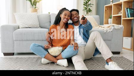 Glückliches schwarzes Paar, das Popcorn isst und einen Film spielt, der in ihrem Wohnzimmer oder Haus spielt. Liebe, Romantik und Mann und Frau haben Freizeit Stockfoto
