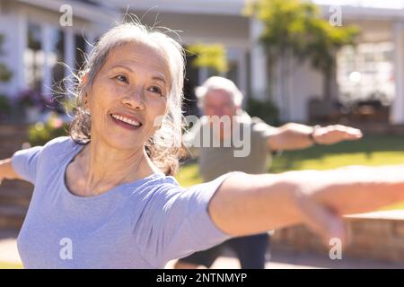 Glückliches, abwechslungsreiches Seniorenpaar, das Yoga macht und sich im Garten streckt Stockfoto