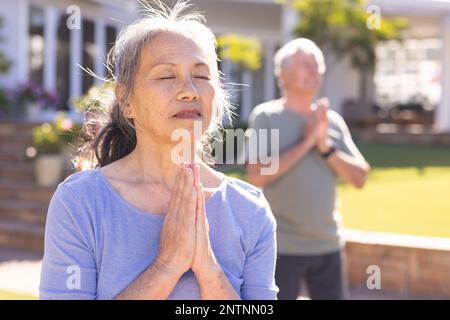 Glückliches, abwechslungsreiches Seniorenpaar, das Yoga macht und im Garten meditiert Stockfoto