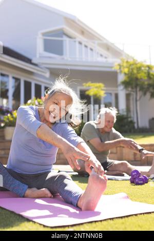 Glückliches, abwechslungsreiches Seniorenpaar, das Yoga macht und sich im Garten streckt Stockfoto
