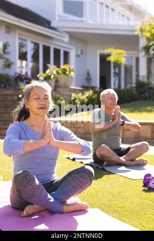 Glückliches, abwechslungsreiches Seniorenpaar, das Yoga macht und im Garten meditiert Stockfoto