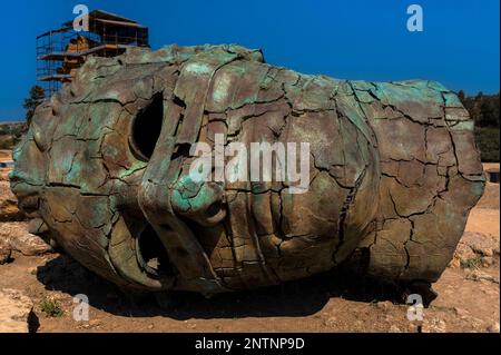 Großer Bronzekopf von Eros, gerissen und mit leeren Augenhöhlen, vom polnischen Bildhauer Igor Mitoraj (1944-2014). Diese Skulptur des altgriechischen Gottes der Liebe und Begierde wurde 2011 im Tal der Tempel in Agrigento, Sizilien, Italien, fotografiert, wo die Skulptur von 2011 bis 2013 auf der Seite lag. Stockfoto
