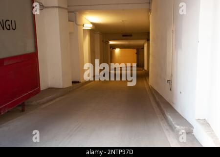 Der Zugang zur Tiefgarage erfolgt über eine weiße Passage, die Tür ist rot. Stockfoto