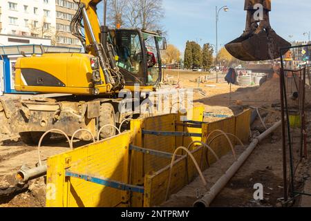 Hydraulikbagger füllt Tiefenaushub, unterstützt durch Grabenkasten mit Rohreinstreu Erbsenkies während der Installation des Entwässerungsrohrs. Rekonstruktion der Technik Stockfoto