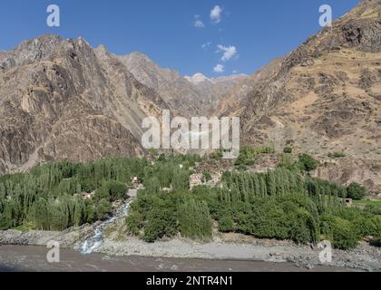 Landschaftsblick auf Bergdorf inmitten von Bäumen und Torrent auf der afghanischen Seite des Panj-Flusstals, Darvaz-Viertel, Gorno-Badakshan, Tadschikistan Pamir Stockfoto