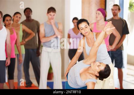 Dies ist die richtige Technik. Ein Yogalehrer, der eine Routine mit einem Kunden in der Klasse vorführt. Stockfoto