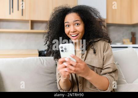 Überglücklich Frau, die auf den Telefonbildschirm schaut und den Erfolg feiert. Aufgeregt zufrieden junge Frau hält Smartphone, lesen gute Nachrichten in Nachricht, Lotterie gewinnen, Shopping-Angebot Stockfoto