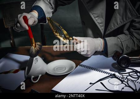 Zugeschnittenes Bild eines männlichen Detektivs, der in einer Lupe auf Fingerabdrücke auf der Kaffeetasse schaut und Hinweise auf Fälle findet. Professionelle Untersuchung Stockfoto