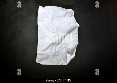 Zerknittertes Papier Draufsicht Nahaufnahme eines zerknitterten Blatts weißes Papier. Draufsicht strukturierter Papierhintergrund, dunkle Betonstruktur. Platz für Text Stockfoto