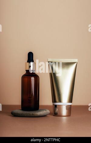 Braune kosmetische Serumflasche und goldfarbenes Röhrchen auf neutralem beigefarbenem Hintergrund. Naturhautpflegekosmetik-Konzept. Modell, Raum kopieren. Stockfoto