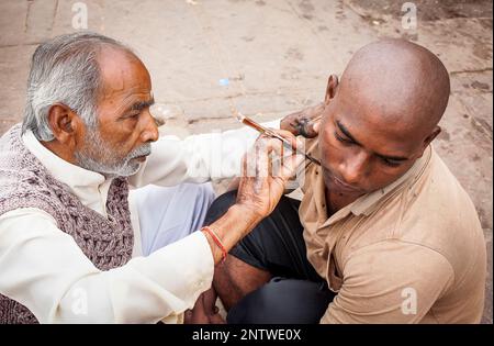 Barbier rasieren des Kopfes und Bart eines Pilgers, Dashashwamedh Ghat (Haupt-Ghat), im Fluss Ganges, Varanasi, Uttar Pradesh, Indien. Stockfoto