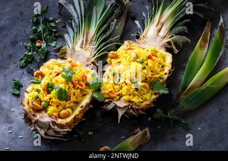 Asiatischer Reis in Ananas mit Eiern, Erbsen, Cashew und Koriander auf dunklem Metallhintergrund. Leckeres orientalisches und thailändisches Gericht Stockfoto