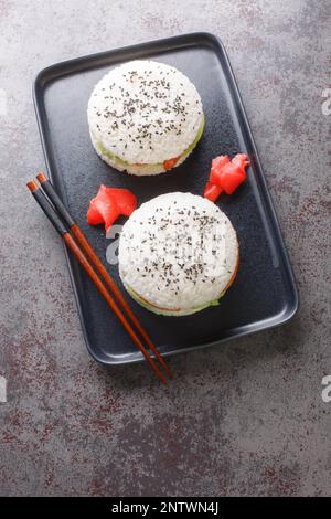 Sushi-Burger mit Avocado und Lachs auf dunklem Hintergrund. Selektiver Fokus. Vertikale Draufsicht von oben Stockfoto