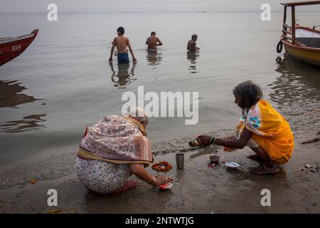 Frauen beten und Opfergaben im Hintergrund Männer Baden Ghats von Fluss Ganges, Varanasi, Uttar Pradesh, Indien. Stockfoto