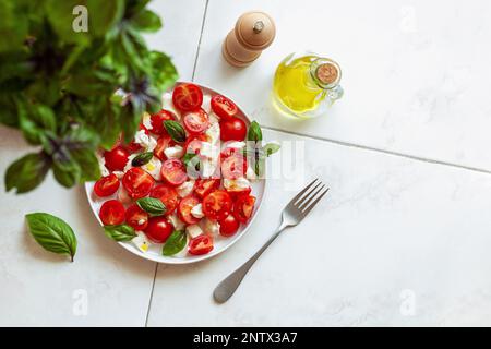 Portion Caprese-Salat unter der Basilikumpflanze, Draufsicht, Copyspace, selektiver Fokus Stockfoto