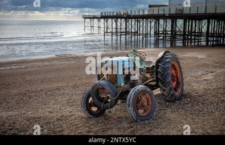 Ein klassischer und verrosteter Traktor, der von einem Fischer benutzt wurde, um sein Boot zu bringen, liegt am Kiesstrand vor dem Bognor Regis Pier in West Sussex, Stockfoto